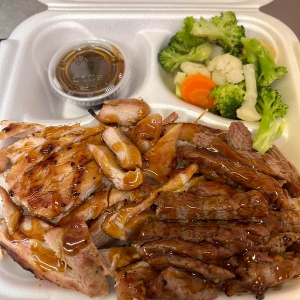 Maui Teriyaki and Sushi's teriyaki chicken and beef with steamed vegetables and sauce in a takeout container.