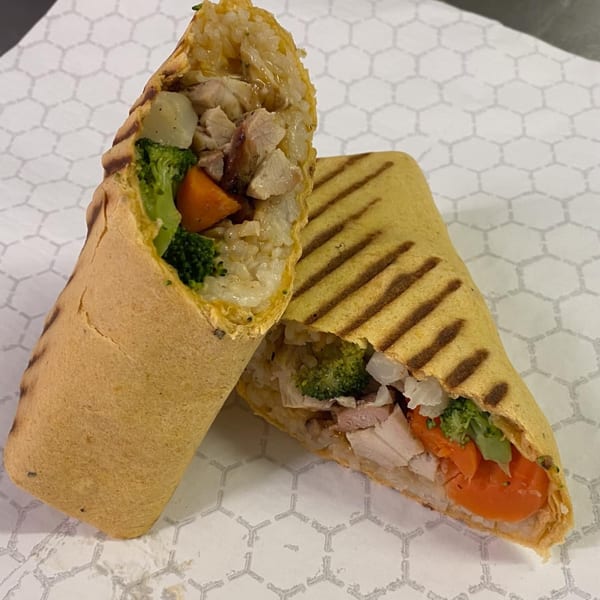 Two halves of a grilled teriyaki chicken and vegetable wrap on white hexagonal patterned paper.